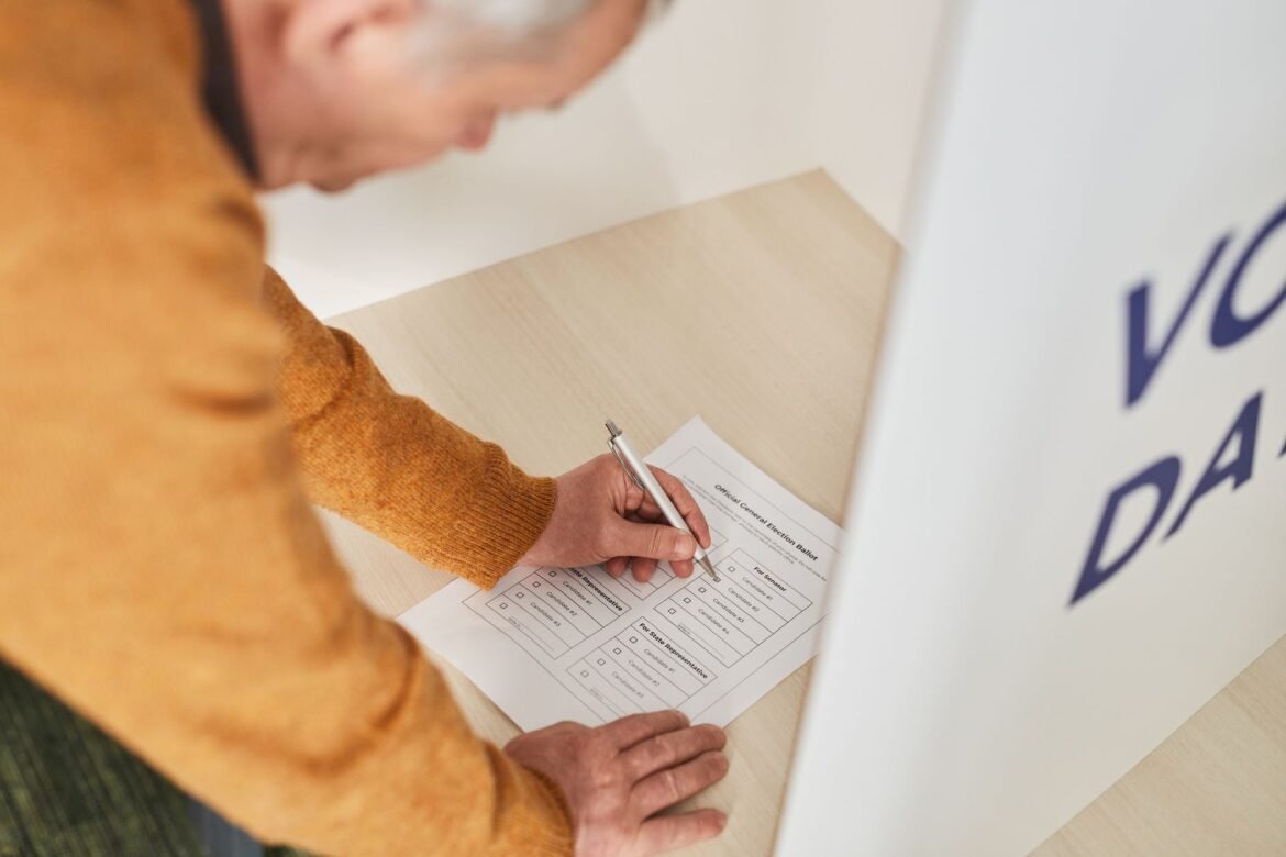 Senior man marking a ballot at a voting booth in an indoor polling station.