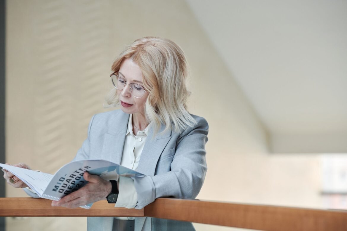Professional Caucasian woman in a gray blazer reading a business report indoors.