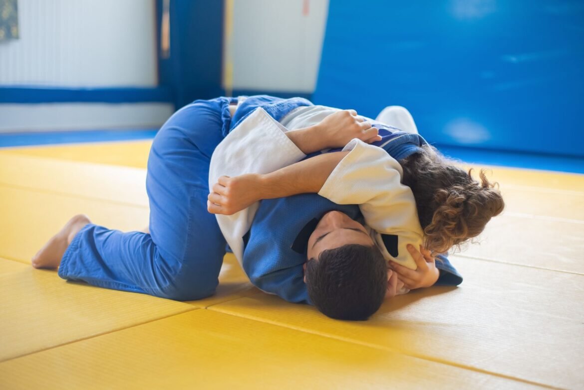 Two athletes practicing judo grappling techniques indoors on a tatami mat.
