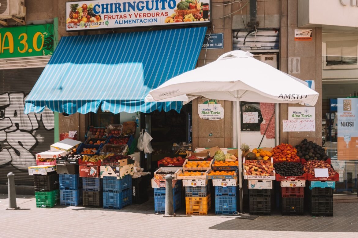 Vibrant outdoor produce store in Valencia displaying fresh fruits under a blue awning.