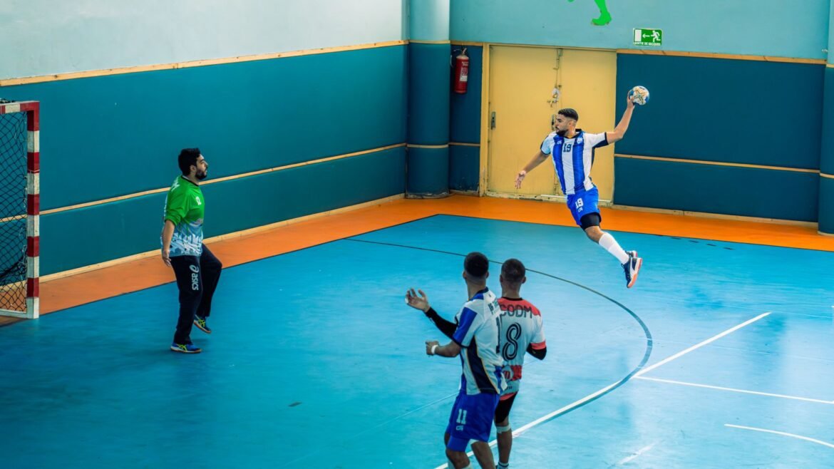 Dynamic handball match with player making a powerful jump shot indoors.