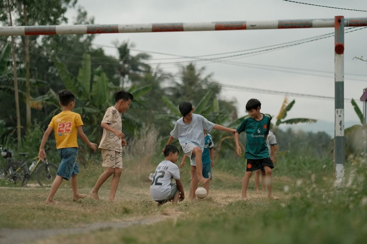 Group of boys playing soccer in a lush green field on a cloudy day.